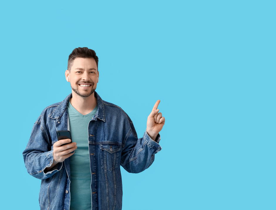 Man with Phone and Earphones Pointing at Something on Color Background
